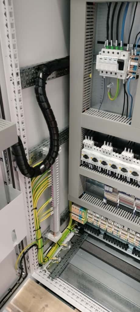 Rozdzielnia elektryczna w trakcie prefabrykacji: widoczne kable w peszlu, listwy zaciskowe i aparatura modułowa. Estetyczne i uporządkowane ułożenie przewodów.