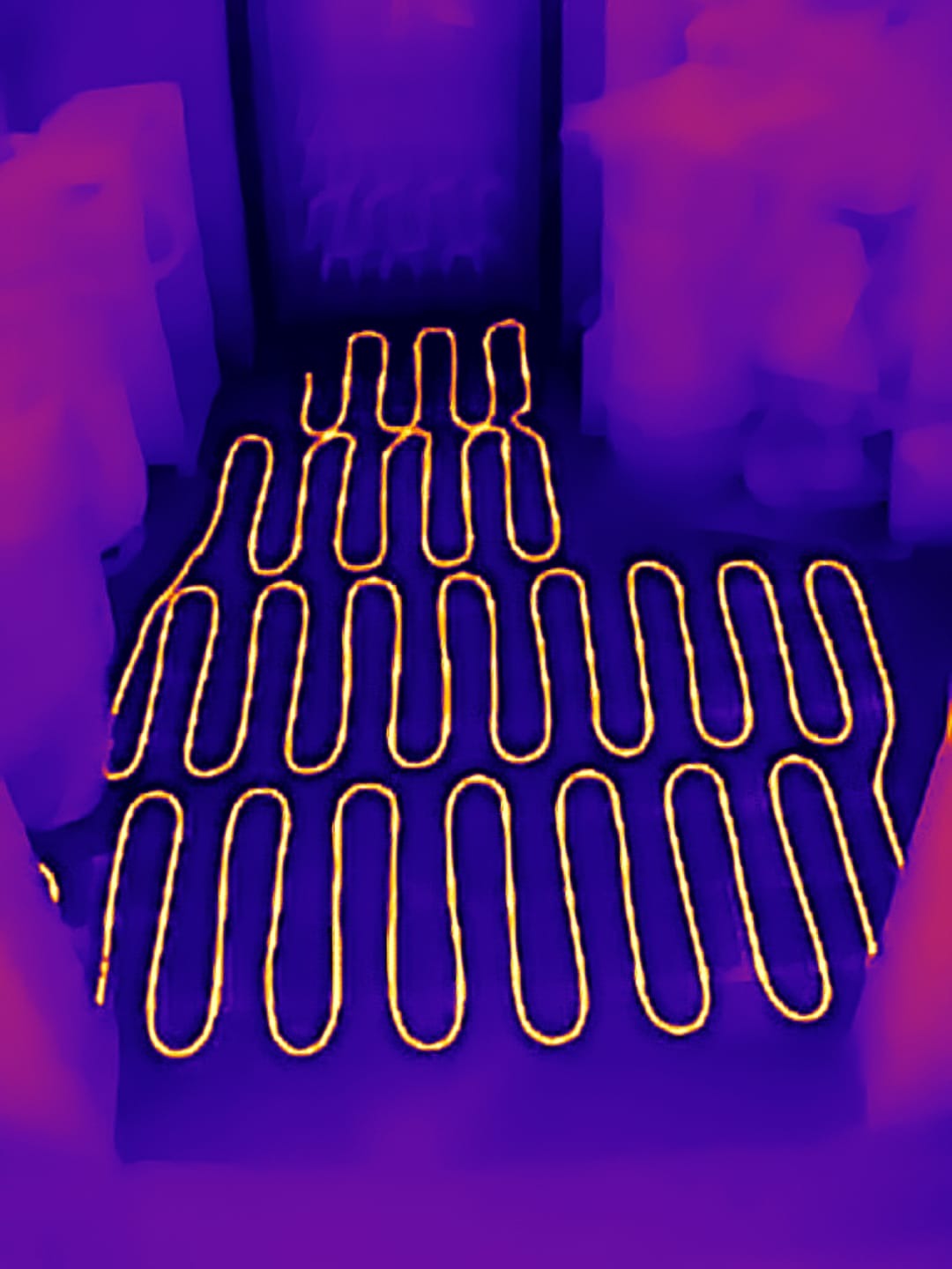 Termowizja: żółta mata grzewcza ułożona zygzakiem na fioletowej podłodze, widok z góry, ciepło rozchodzi się równomiernie.