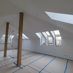 Dmytro Nahurnyi - Poddasze po gładziowaniu i malowaniu na biało, z widocznymi oknami dachowymi i zabezpieczoną podłogą. Dwie drewniane kolumny podtrzymują strop.