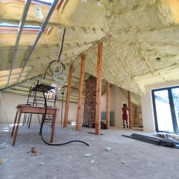Dmytro Nahurnyi - Poddasze w trakcie izolacji pianą PUR. Widoczne drewniane słupy, okna dachowe i fragment muru z cegły. Na podłodze resztki piany i narzędzia.