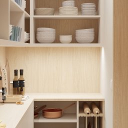ZMYSŁ WNĘTRZA Architektura Roksana Simińska - Jasna spiżarnia z drewnianymi półkami, na których stoją naczynia, garnki miedziane i akcesoria kuchenne. Minimalistyczny design, ciepłe oświetlenie.
