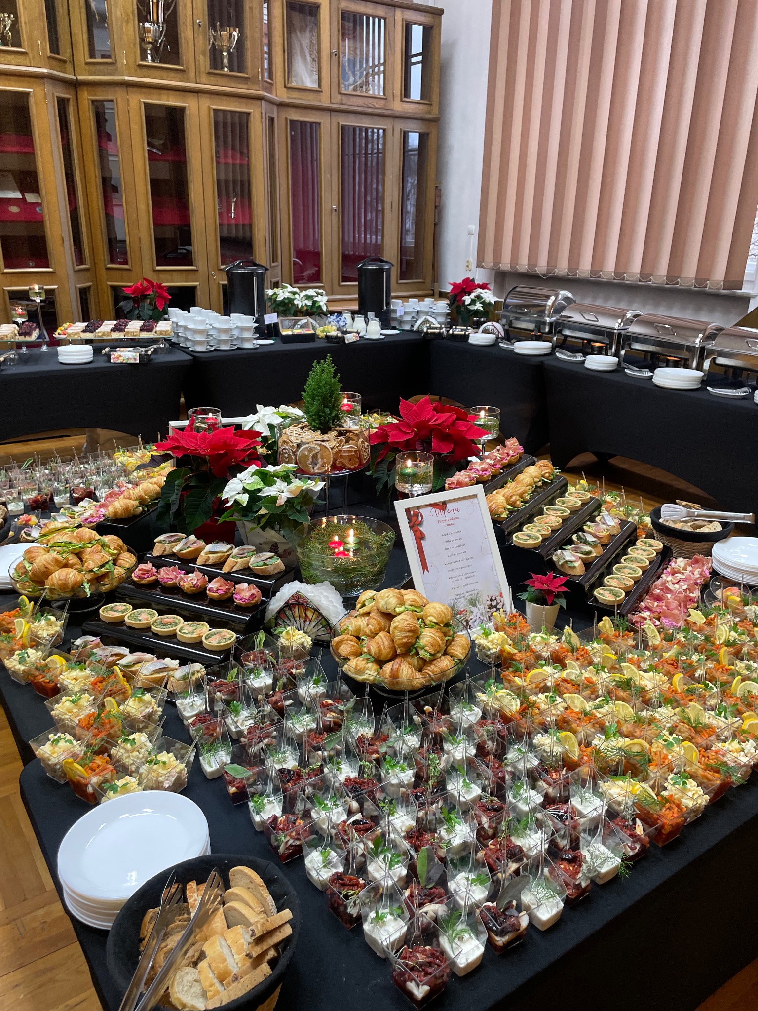 Bogato zastawiony stół cateringowy z przekąskami, dekoracjami świątecznymi i menu w eleganckim wnętrzu z drewnianymi meblami.