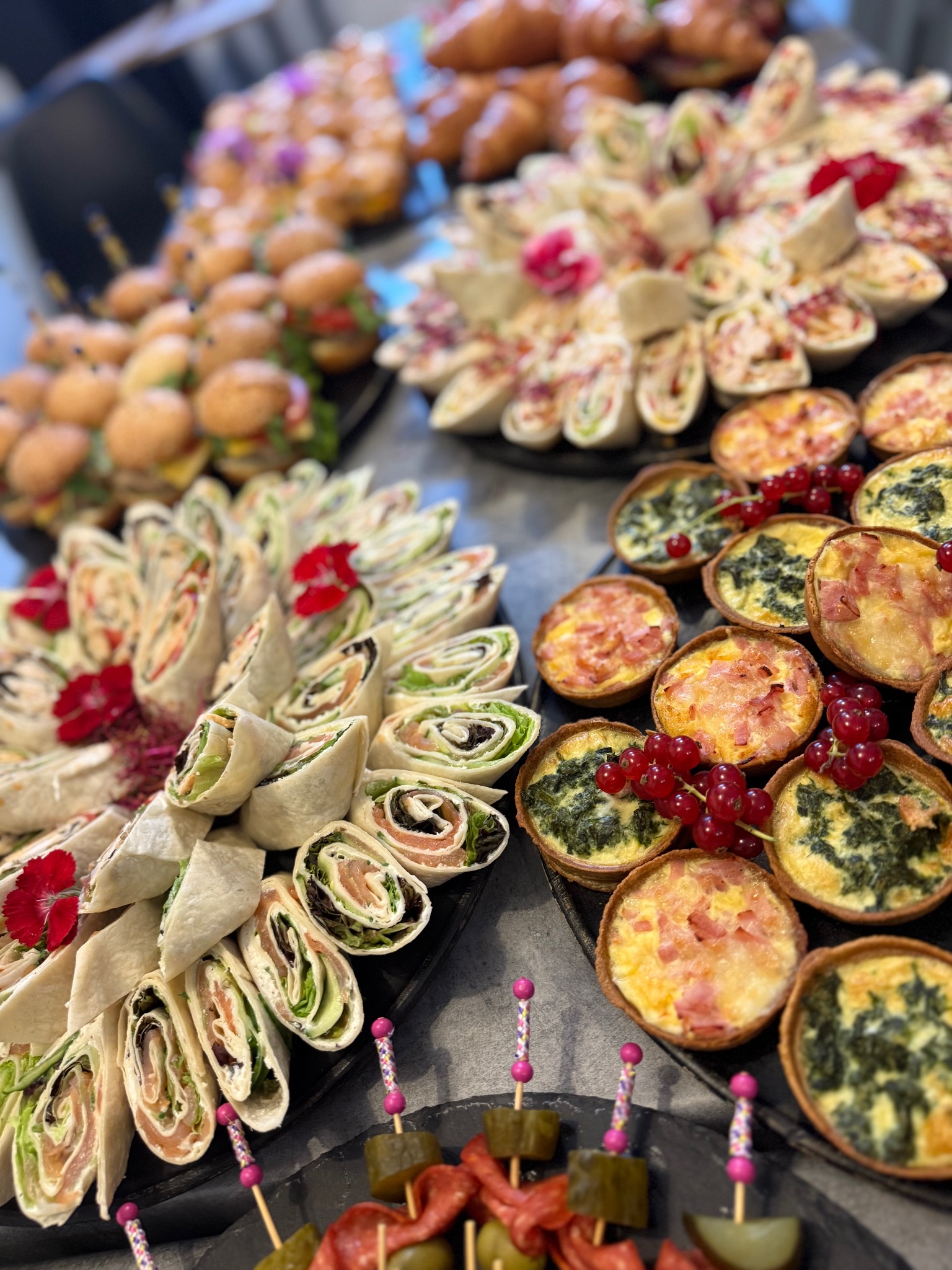 Elegancki catering: mini tortille z łososiem, quiche z warzywami i szynką, mini burgery i rogaliki na czarnych tacach, idealne na imprezy firmowe i świąteczne.