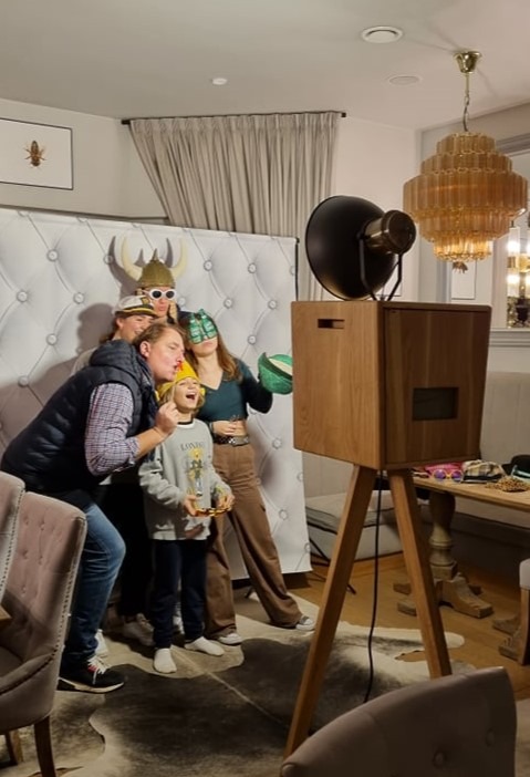 Rodzinne zdjęcie w fotobudce retro z rekwizytami: hełmy wikingów, maski i okulary. W tle dekoracyjna ściana i żyrandol.