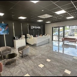 Skin-Medic klinika medycyny estetycznej (Klinika AK sp z oo) - Nowoczesne wnętrze salonu kosmetycznego: recepcja, strefa oczekiwania z fotelami i TV prezentującym zabieg, czarno-biała kolorystyka, marmurowa podłoga.