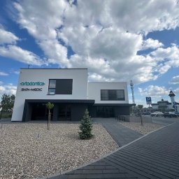 Skin-Medic klinika medycyny estetycznej (Klinika AK sp z oo) - Nowoczesny budynek kliniki ortodontyczno-medycznej z nazwą 'ortodontica SKIN-MEDIC' na elewacji, otoczony zielenią i parkingiem w słoneczny dzień.