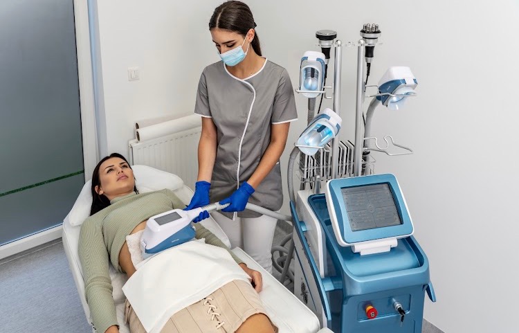 Kobieta poddaje się zabiegowi kriolipolizy na brzuchu w gabinecie medycyny estetycznej. Kosmetolog w uniformie i rękawicach obsługuje urządzenie.