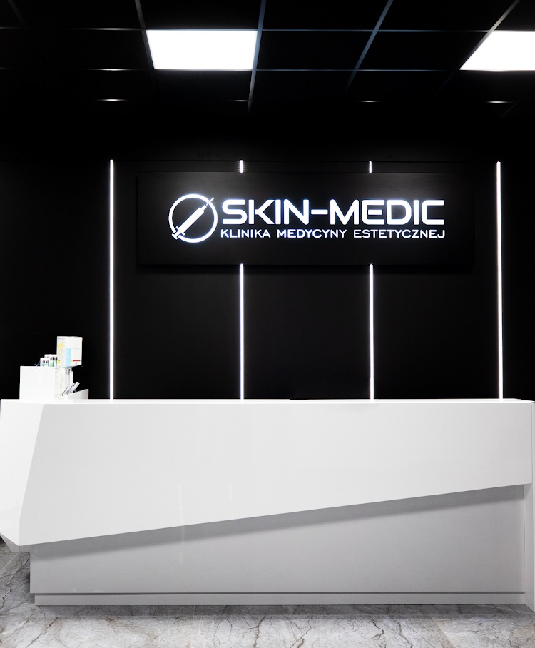 Recepcja kliniki medycyny estetycznej Skin-Medic z logo i podświetleniem LED na czarnym tle. Nowoczesny design, biały blat, marmurowa podłoga.
