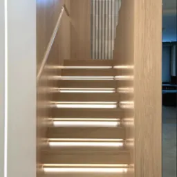 Nowoczesne drewniane schody z podświetleniem LED, widok z dołu. Minimalistyczny design z elementami drewna i bieli. Widoczne detale wykończenia.