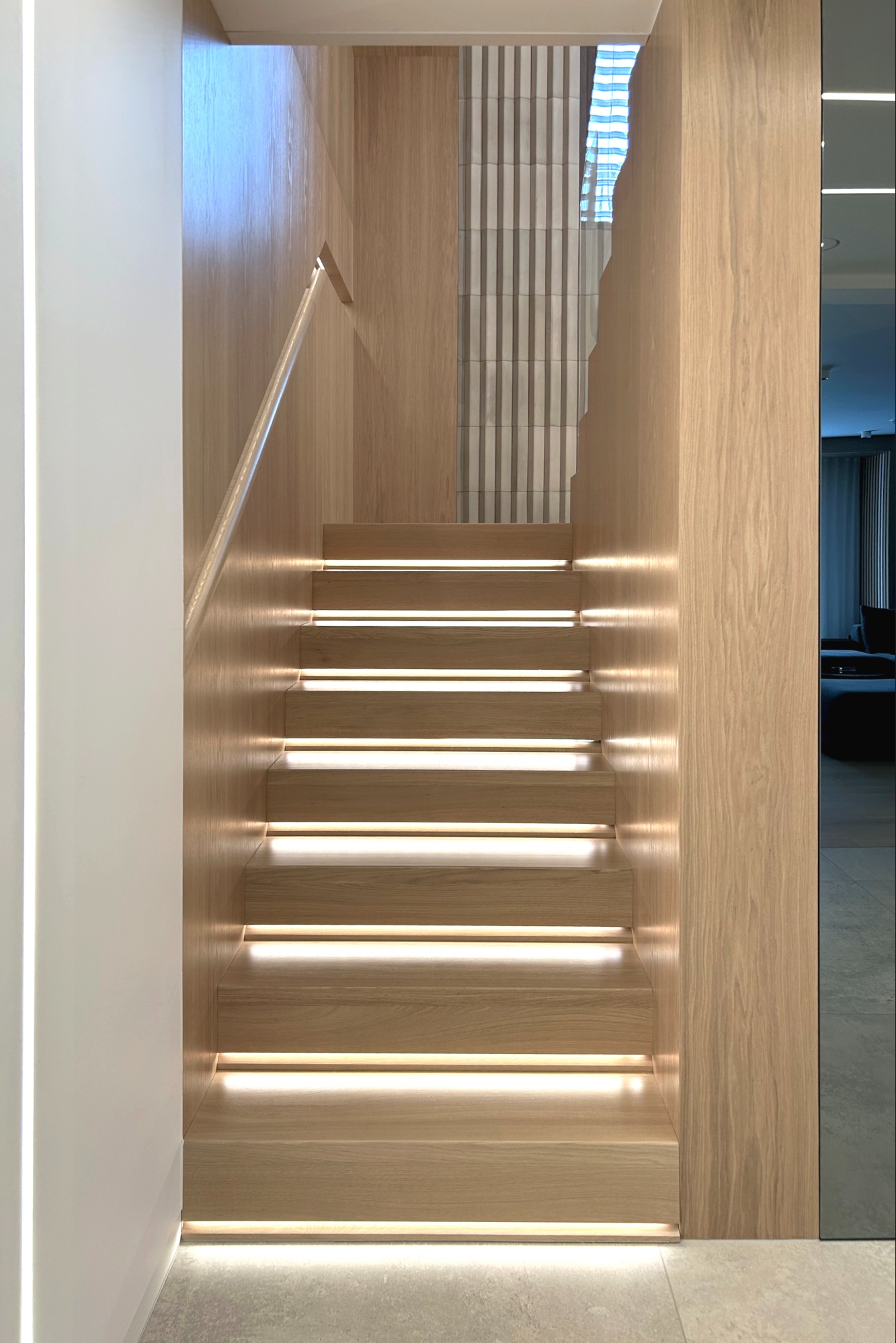 Nowoczesne drewniane schody z podświetleniem LED, widok z dołu. Minimalistyczny design z elementami drewna i bieli. Widoczne detale wykończenia.