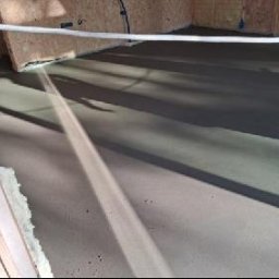 TYNK - BET JUSTYNA SZCZESNA - Świeżo wylana, gładka posadzka jastrychowa w surowym wnętrzu. Widoczne ściany z płyt OSB i izolacja. Cień rzucany przez przewód na posadzce.