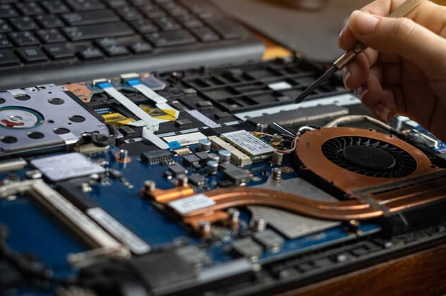 Otwarty laptop z widoczną płytą główną, gdzie dłoń z precyzyjnym śrubokrętem dokonuje naprawy układu chłodzenia, wentylatora.