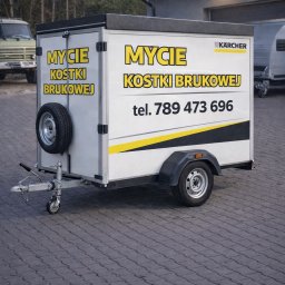 Przyczepa z reklamą firmy Karcher oferującej mycie kostki brukowej, zaparkowana na kostce brukowej. Widoczny numer telefonu kontaktowego.
