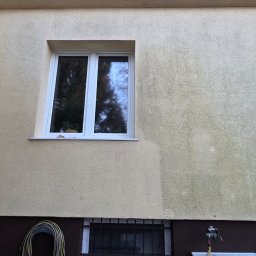 Patrex Patryk Bejynka - Fragment elewacji budynku z widocznym efektem mycia: czysta powierzchnia kontrastuje z zabrudzoną. Okno z białymi ramami, w tle zieleń. Wąż ogrodowy i kran przy ścianie.