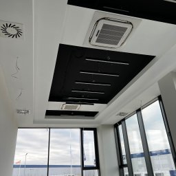 VOSER Sp. z o.o. - Nowoczesny sufit podwieszany z klimatyzacją i oświetleniem w biurze w Szczecinie. Widoczne duże okna i grzejniki. Minimalistyczny design.