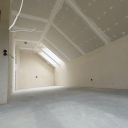 VOSER Sp. z o.o. - Poddasze po montażu płyt na skosach i suficie, widoczne łączenia płyt przygotowane do dalszych prac. W tle okno dachowe i fragment ściany z instalacją elektryczną.