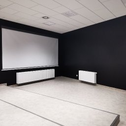 VOSER Sp. z o.o. - Nowoczesne wnętrze biurowe z czarnymi ścianami, ekranem projekcyjnym i panelami akustycznymi. Minimalistyczny design, jasna podłoga i białe grzejniki.