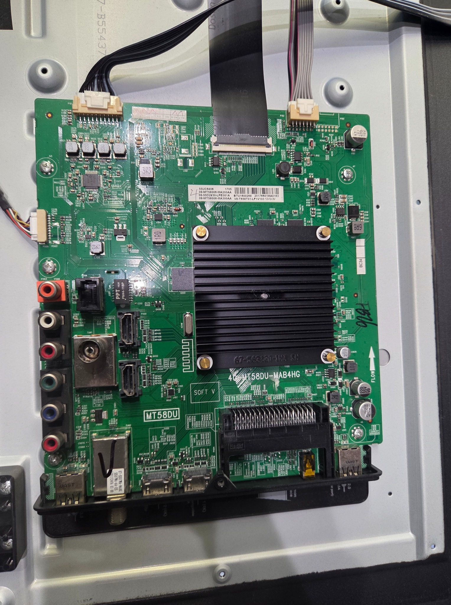 Wnętrze telewizora z widoczną zieloną płytą główną (MT58DU-MAB4HG), liczne układy scalone, złącza i czarne radiatory. Widoczne kable i oznaczenia na płycie.