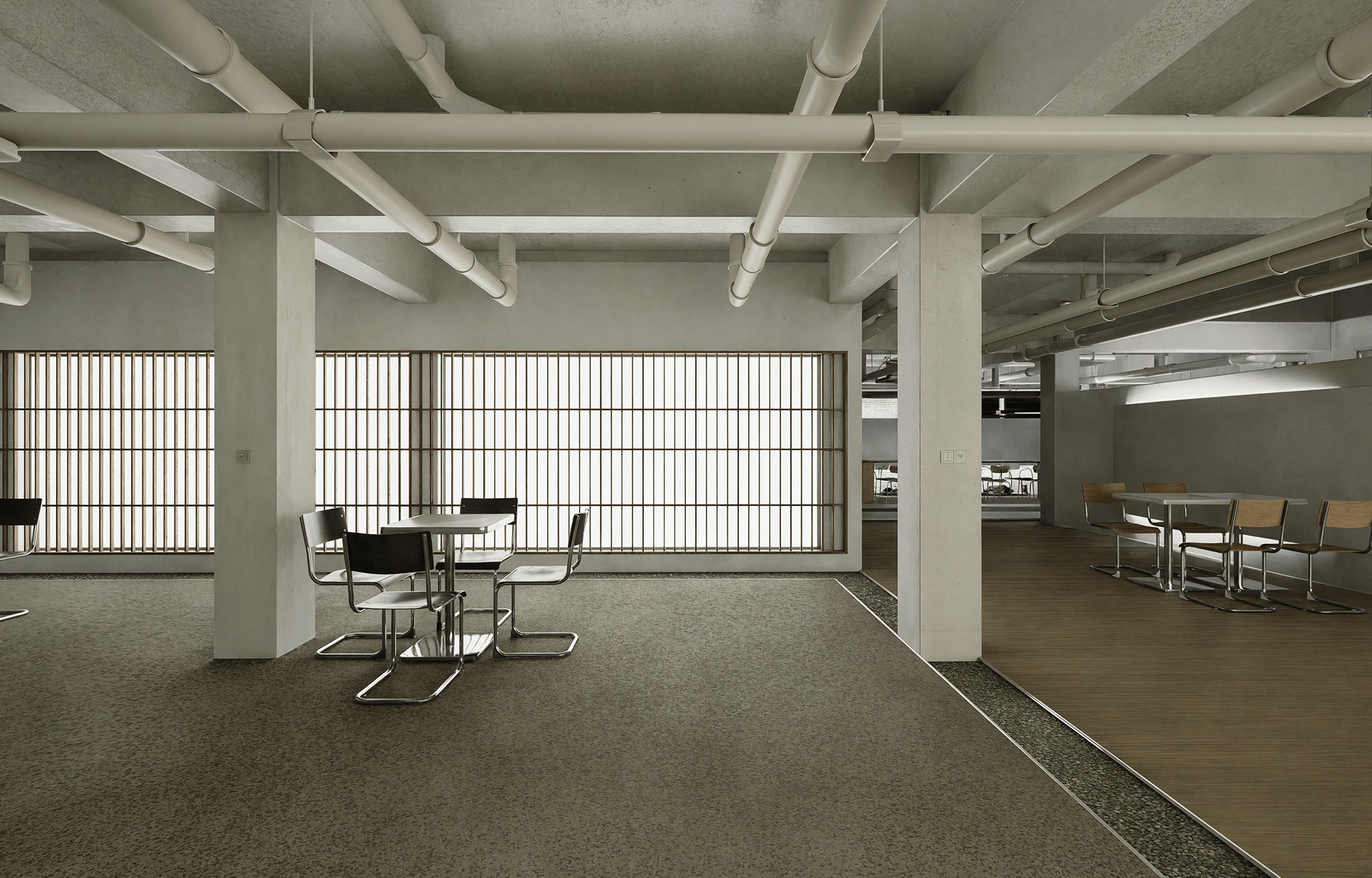 Minimalistyczna aranżacja biura: surowy beton, rzędy rur pod sufitem, stoliki z krzesłami. Duże okna z żaluzjami wpuszczają światło. Podłoga z wykładziną.