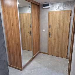 Tarka term Łukasz Tarka - Nowoczesny przedpokój z drewnianą szafą przesuwną z lustrem i drzwiami wejściowymi o podobnym wykończeniu, szare ściany i podłoga z płytek imitujących marmur.