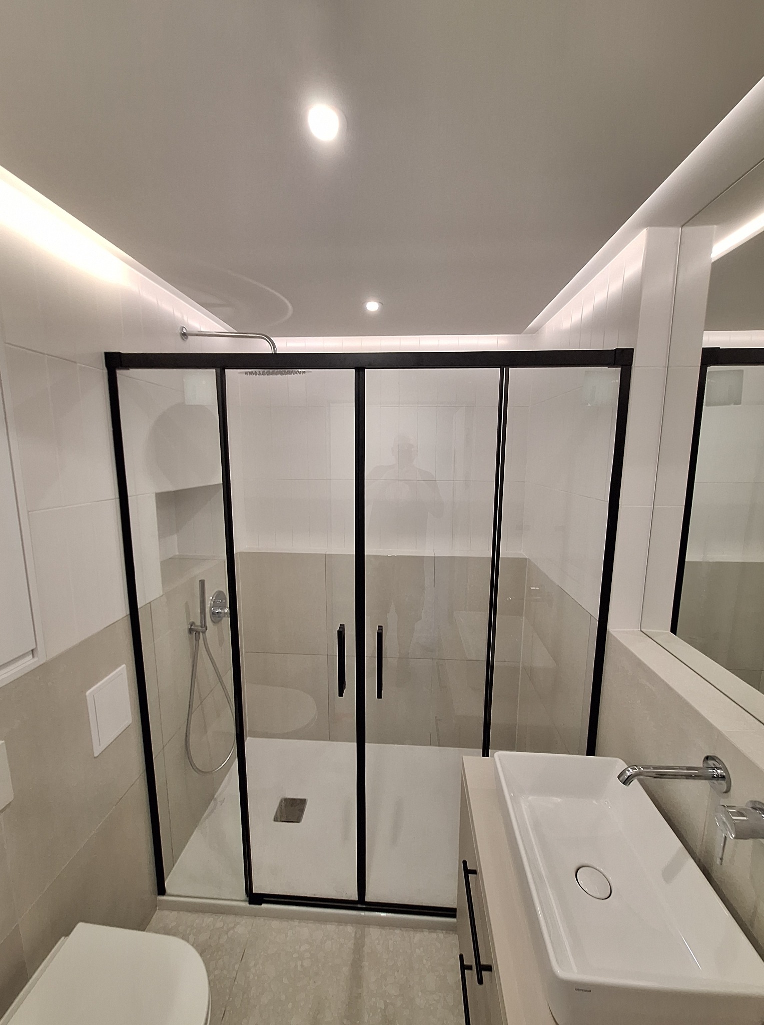 Nowoczesna łazienka po remoncie: kabina prysznicowa z czarnymi ramami, umywalka nablatowa i oświetlenie LED w suficie. Minimalistyczny design i neutralna kolorystyka.