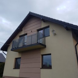 Dziedzic Team - Nowoczesny balkon z metalową balustradą w domu jednorodzinnym, widok z dołu. Balustrada pozioma, szara. Na ścianie antena satelitarna. Drabina oparta o ścianę.