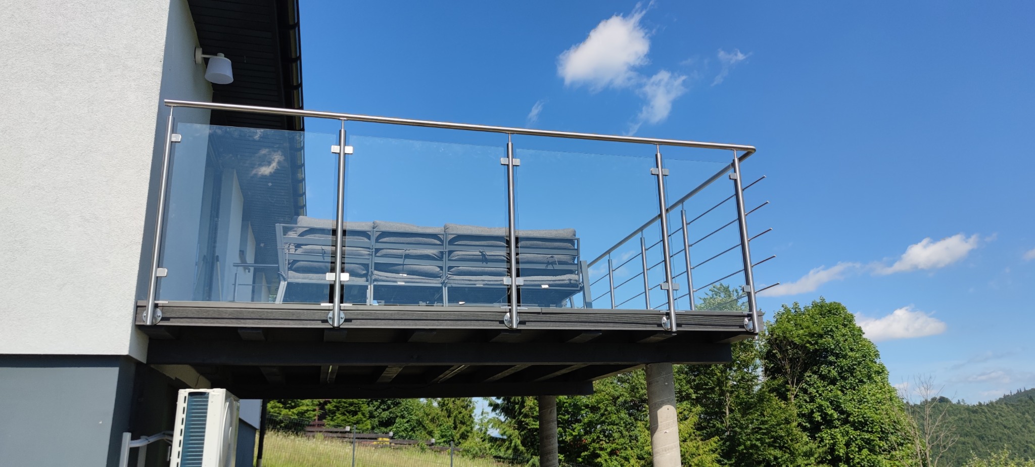 Nowoczesny balkon z balustradą ze stali nierdzewnej i szkła, widok z dołu na tle błękitnego nieba. Minimalistyczny design, metalowe elementy i szklane panele.