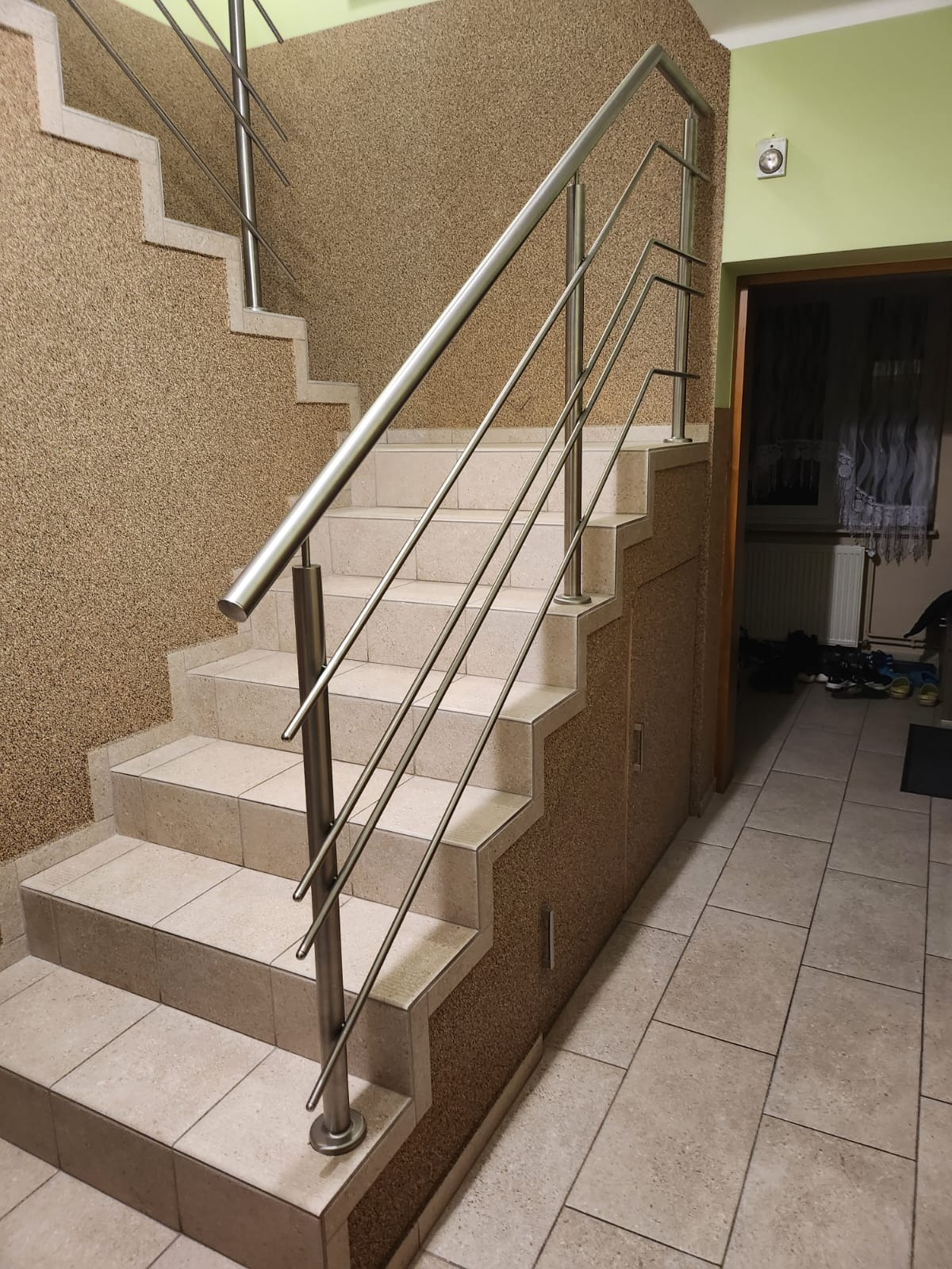 Wnętrze: schody wyłożone jasnymi płytkami z zamontowaną nowoczesną, metalową balustradą z rurek. Ściany pokryte dekoracyjnym tynkiem w odcieniach beżu i brązu.