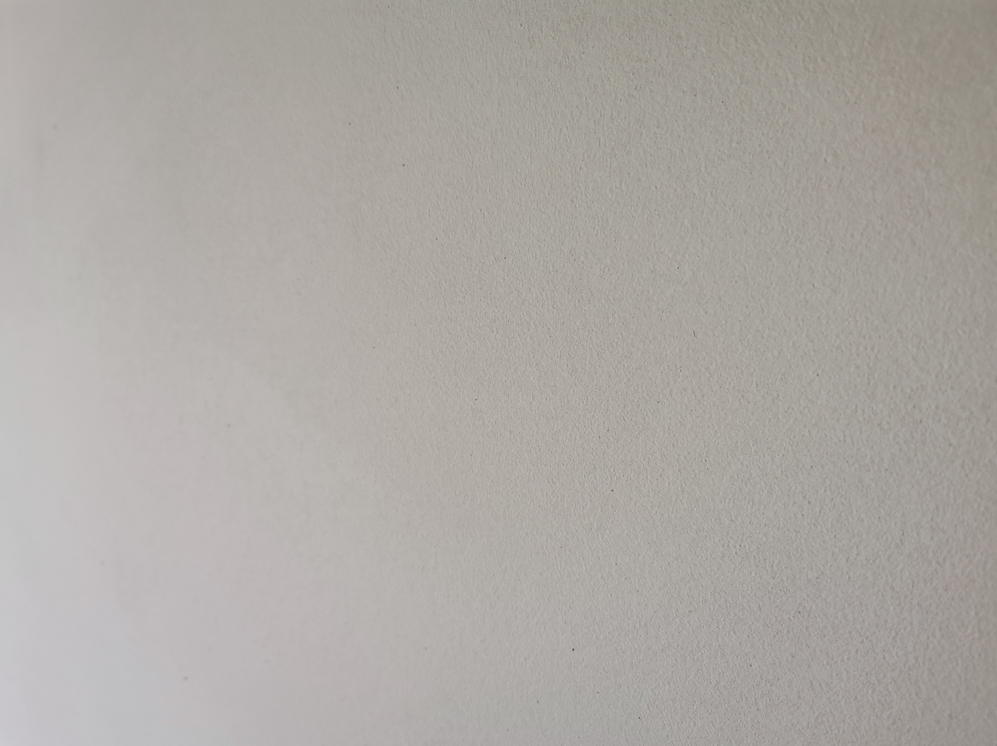 Gładka, jasnoszara powierzchnia ściany po nałożeniu tynku. Delikatna faktura, równomierne wykończenie. Minimalistyczny detal ściany.