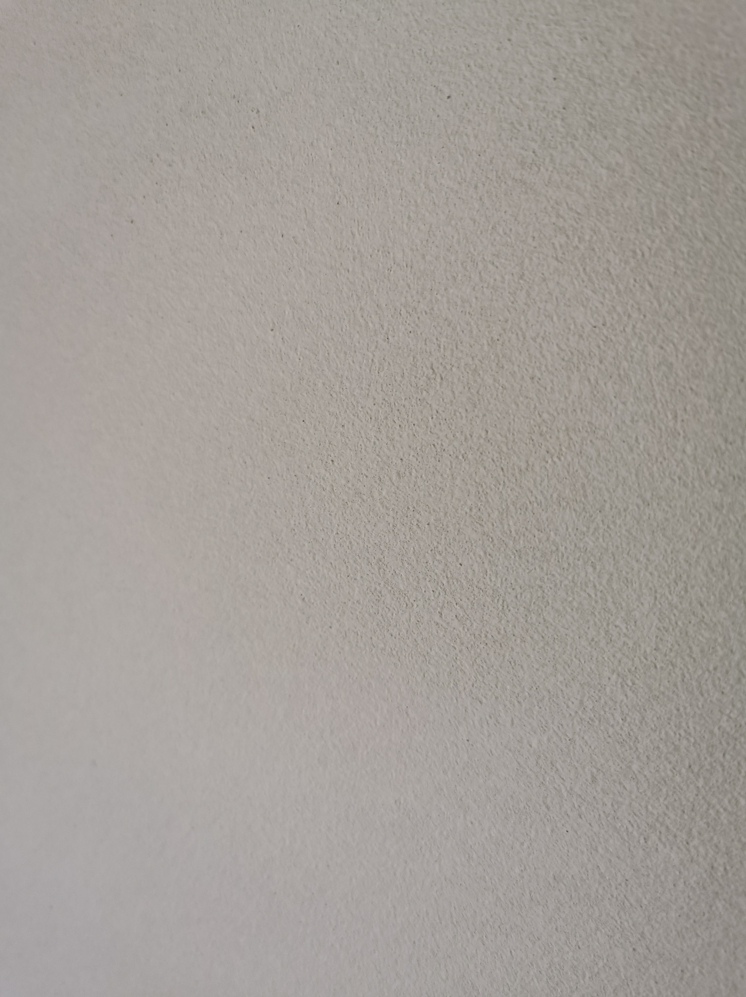 Gładka, jasnoszara powierzchnia tynku maszynowego z delikatną fakturą, oświetlona z lewej strony, ukazująca równomierne wykończenie ściany.