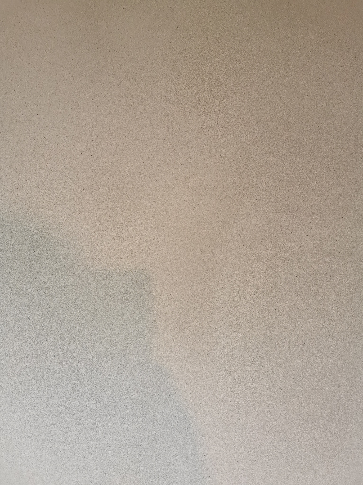 Gładka, beżowa ściana z delikatną fakturą, oświetlona z prawej strony, tworząca subtelny cień. Minimalistyczne wykończenie wnętrza.