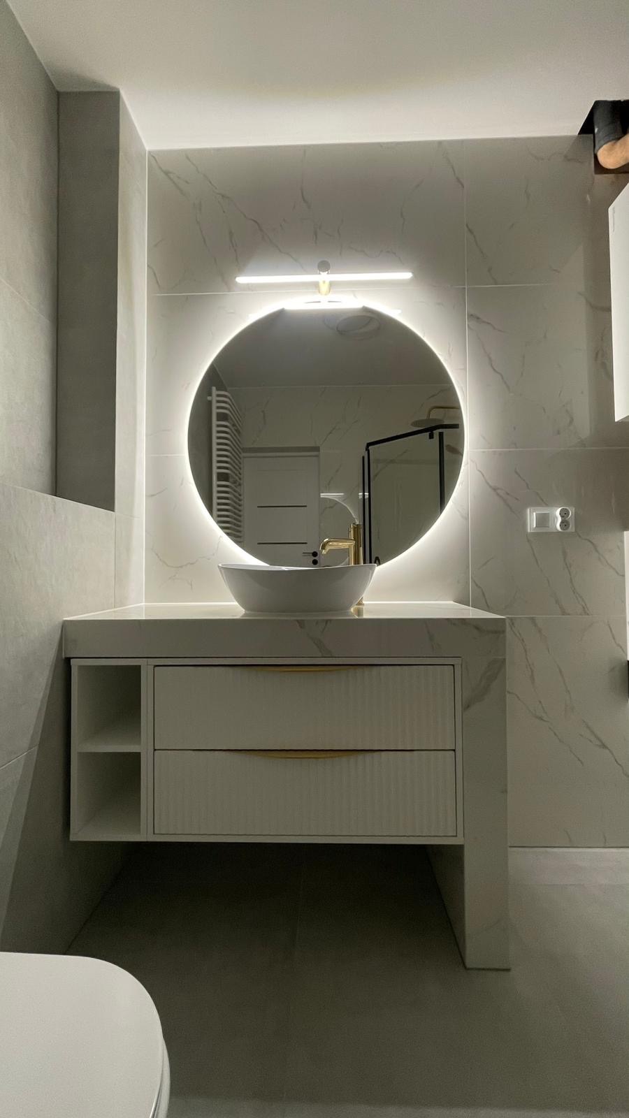 Nowoczesna łazienka z umywalką nablatową, okrągłym lustrem z podświetleniem LED i szafką z frezowanymi frontami. Marmurowe płytki na ścianach i podłodze.