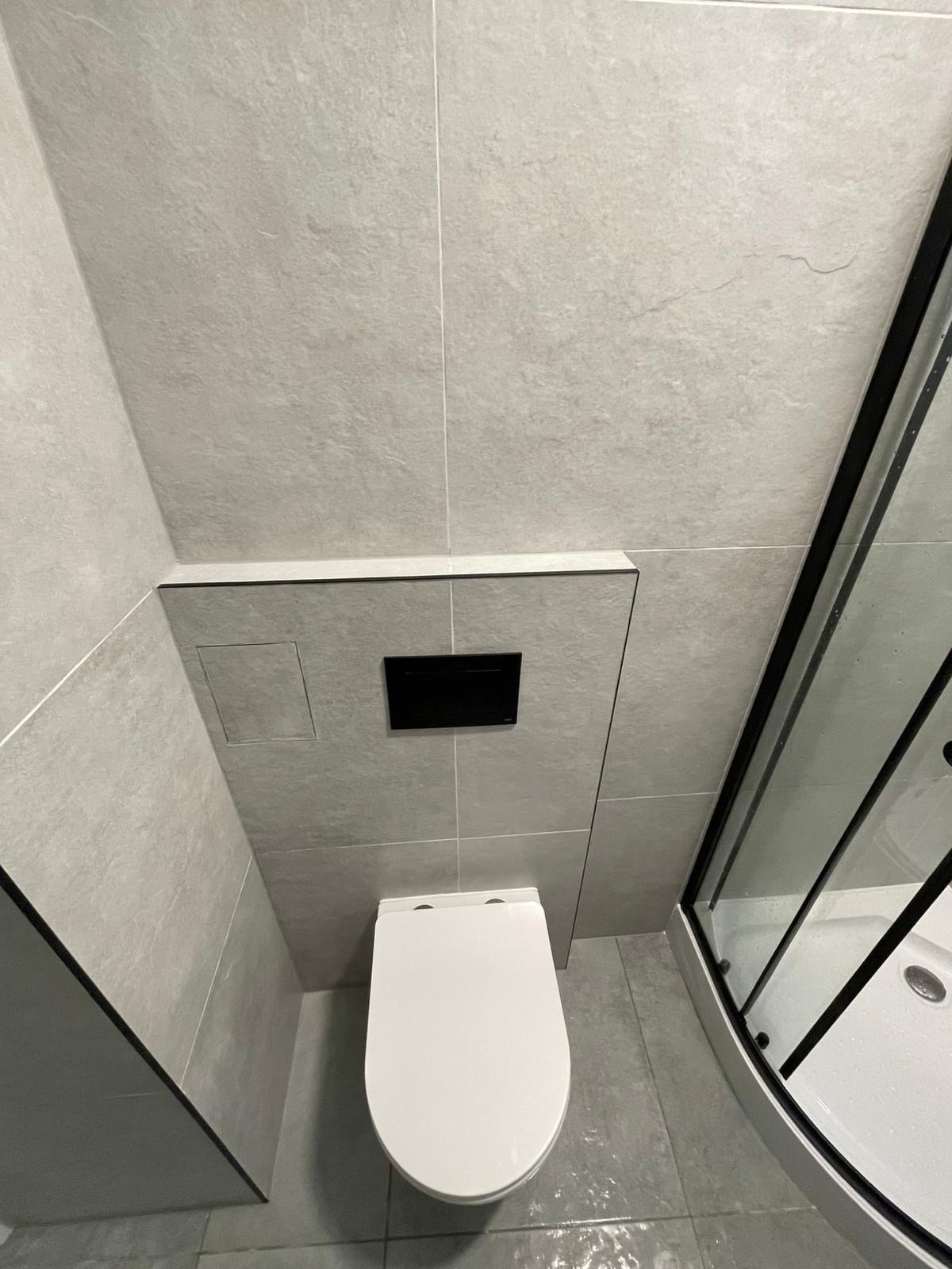 Nowoczesna toaleta w szarościach: podwieszana miska WC, szklana kabina prysznicowa z czarnymi profilami, szare płytki. Minimalistyczny design.