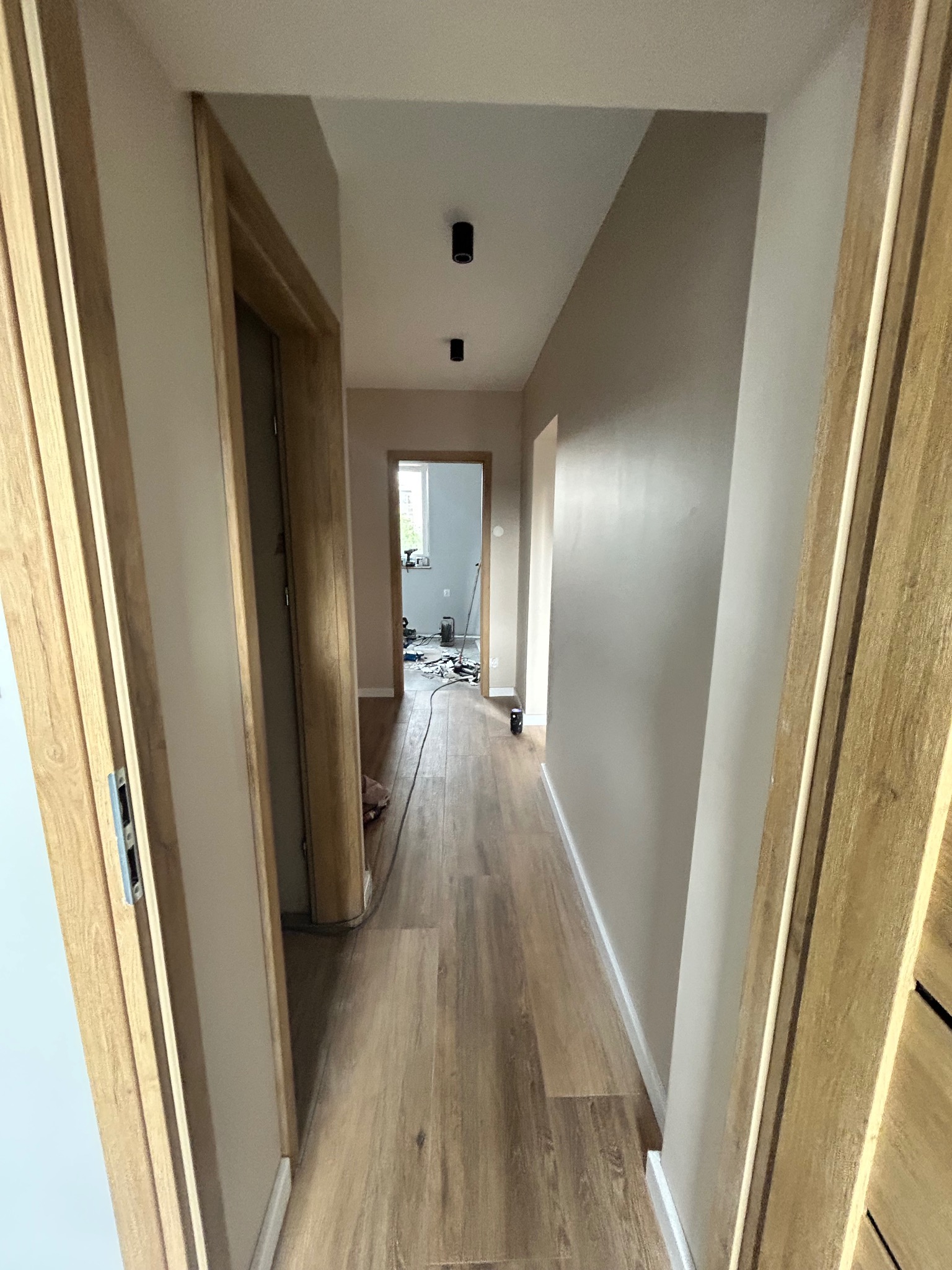 Jasny przedpokój po remoncie: drewnopodobna podłoga, świeżo pomalowane ściany w odcieniach beżu, widoczne ościeżnice drzwiowe z naturalnego drewna.