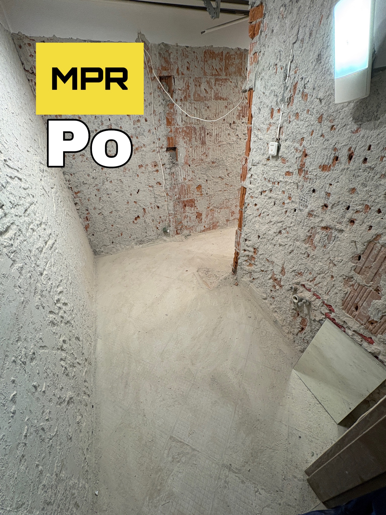 Wnętrze po rozbiórce: odsłonięta cegła, ściany i podłoga pokryte resztkami tynku. Widoczne instalacje. Na zdjęciu widnieje napis 'PO' i logo firmy.
