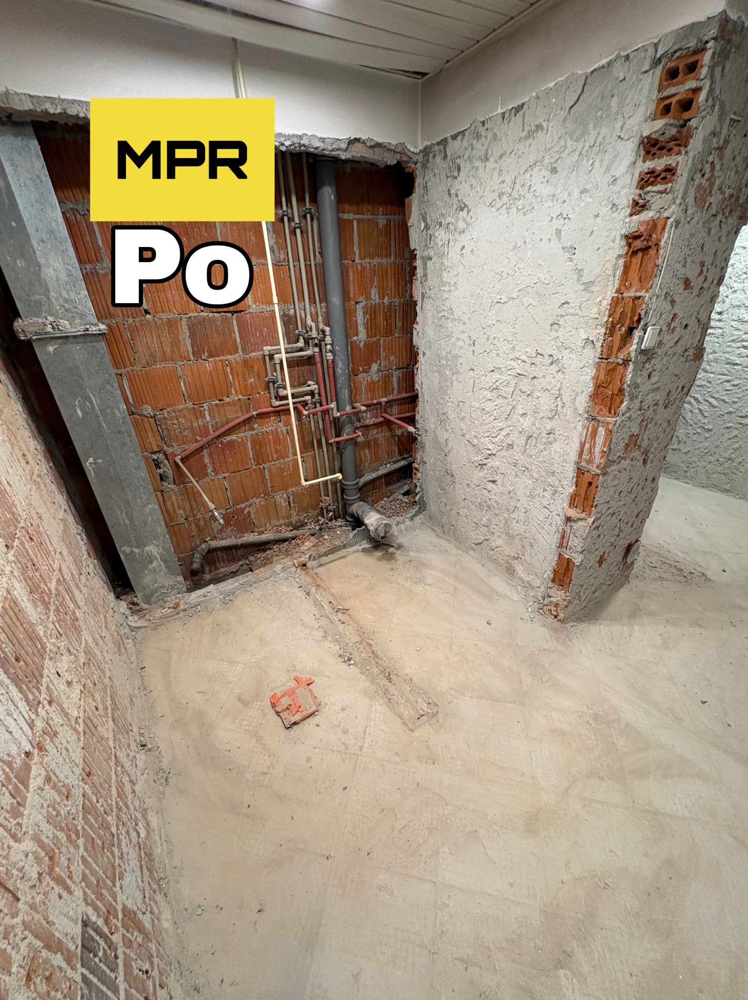 Ceglana ściana po usunięciu tynku, z widocznymi instalacjami. Fragment ściany z cegieł i resztkami tynku. Na podłodze gruz i fragment cegły. Oznaczenie 'MPR Po'.