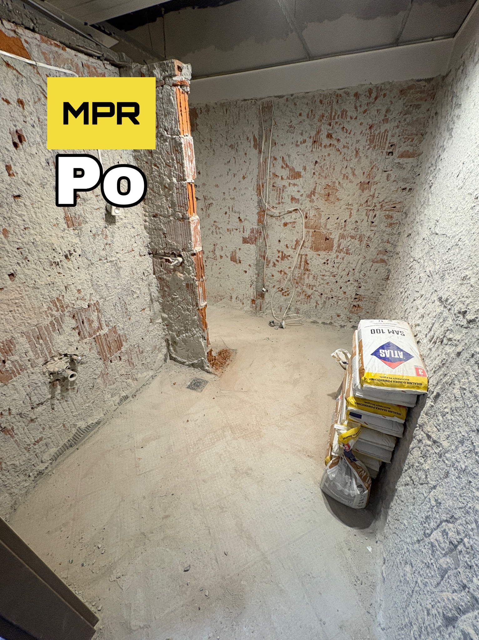 Efekt 'Po' rozbiórki ściany w Warszawie. Odsłonięta cegła, widoczne instalacje, worki z zaprawą Atlas SAM 100. Surowe wykończenie, przygotowanie do dalszych prac.