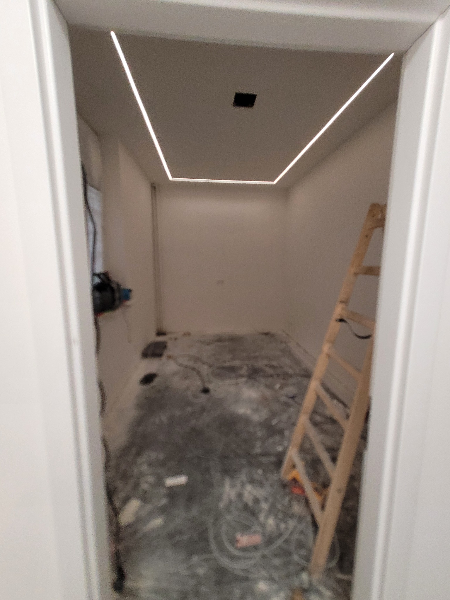 Wnętrze pokoju w trakcie montażu oświetlenia liniowego LED na suficie, widoczna drabina i przewody na podłodze. Nowoczesne rozwiązanie oświetleniowe.