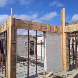 RAFTECH - Budowa domu z białych bloczków: ściany w trakcie wznoszenia, drewniane szalunki podtrzymywane przez metalowe stemple, błękitne niebo w tle. Etap surowy otwarty.