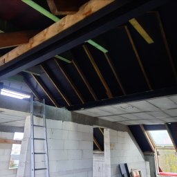 RAFTECH - Poddasze w trakcie adaptacji: widoczne krokwie, izolacja, ściany z betonu komórkowego i drabina. Okno dachowe w tle. Etap prac wykończeniowych.