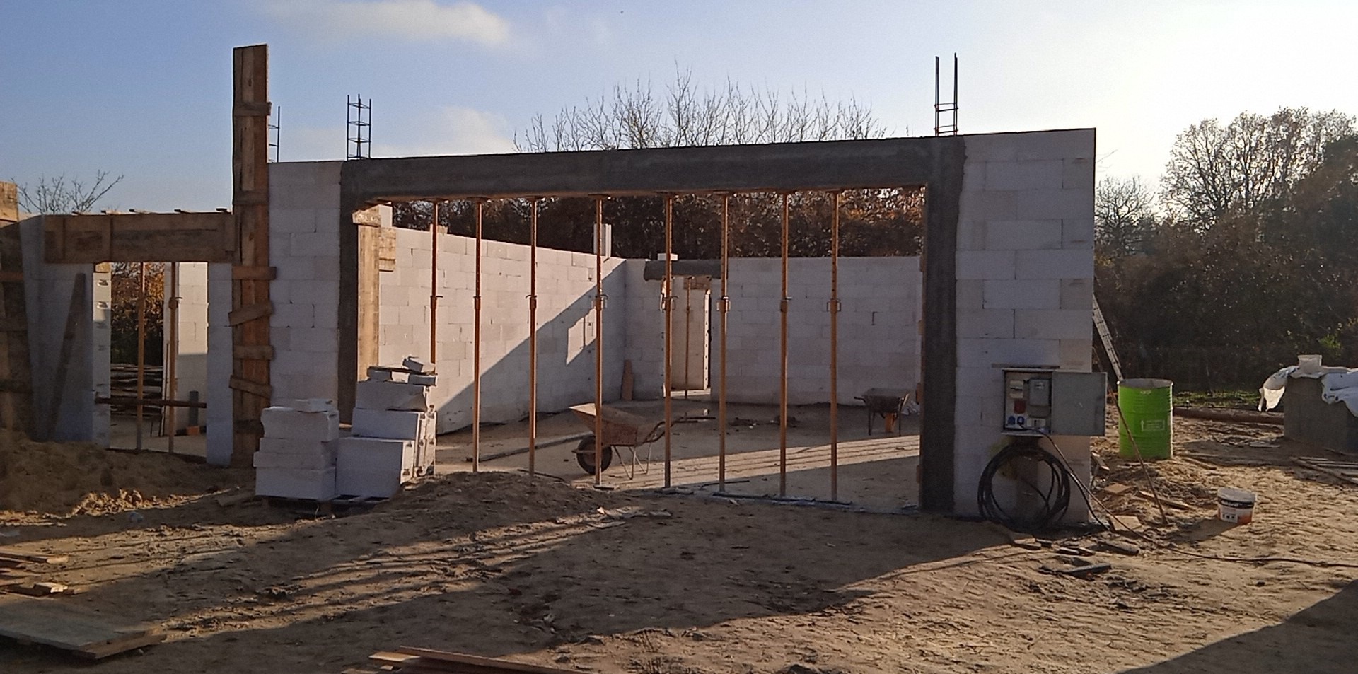 Wznoszenie ścian domu z betonu komórkowego. Widoczne podpory stropu, bloczki, instalacja elektryczna i narzędzia na placu budowy w słoneczny dzień.