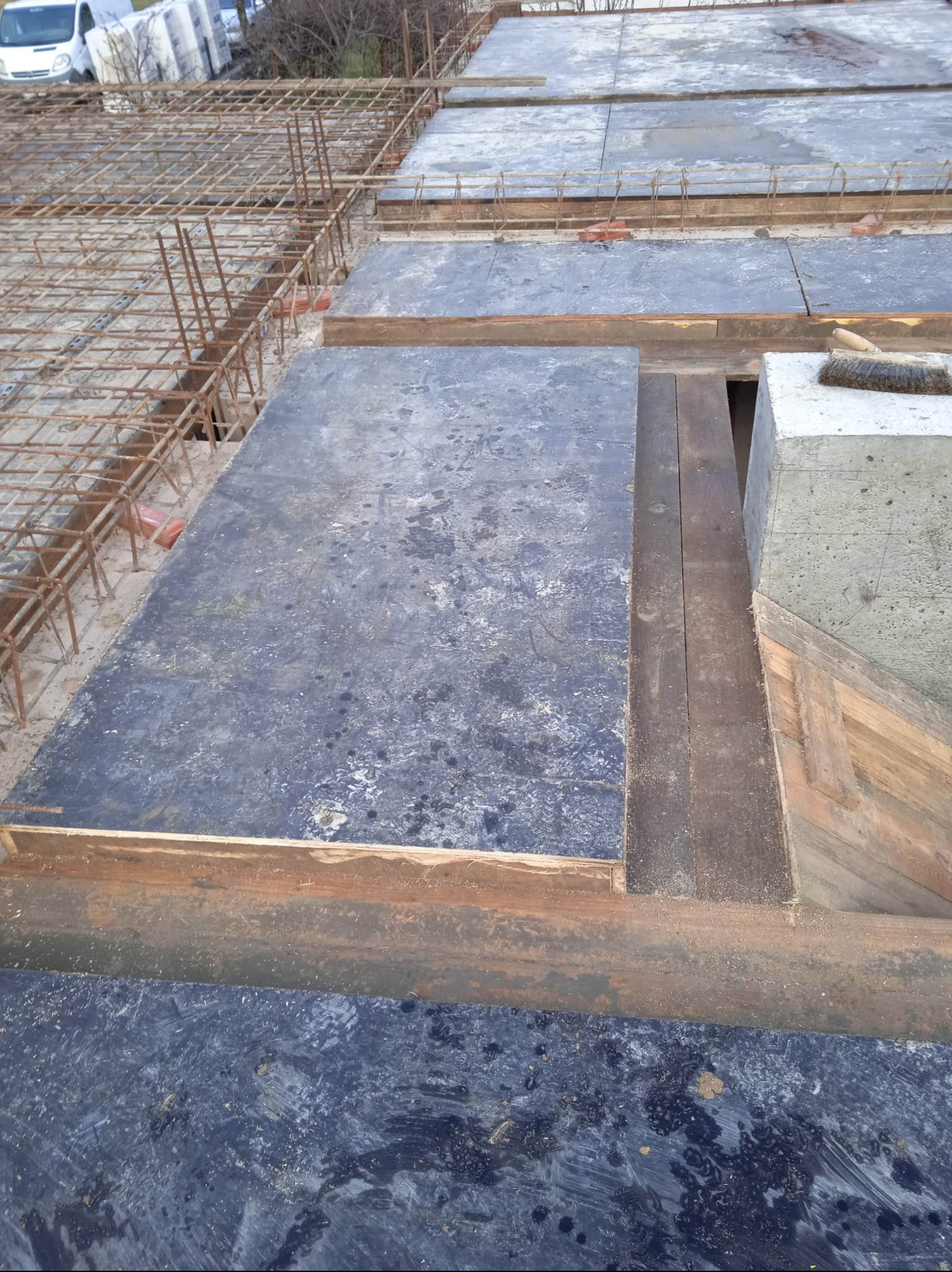 Szczegółowe ujęcie szalunku stropowego z widocznym zbrojeniem i betonowym słupem, przygotowanego do wylania betonu. Widoczne deski i metalowe elementy konstrukcyjne.