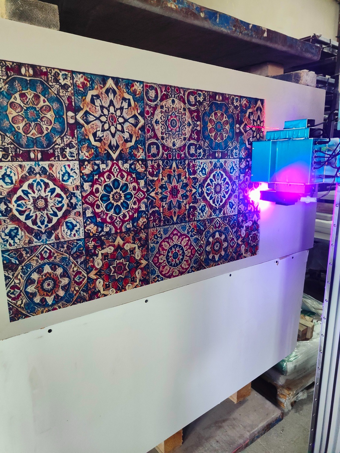 Wielkoformatowa drukarka UV w procesie nadruku wzoru płytek ceramicznych na panel. Widoczna głowica drukująca i intensywne fioletowe światło.