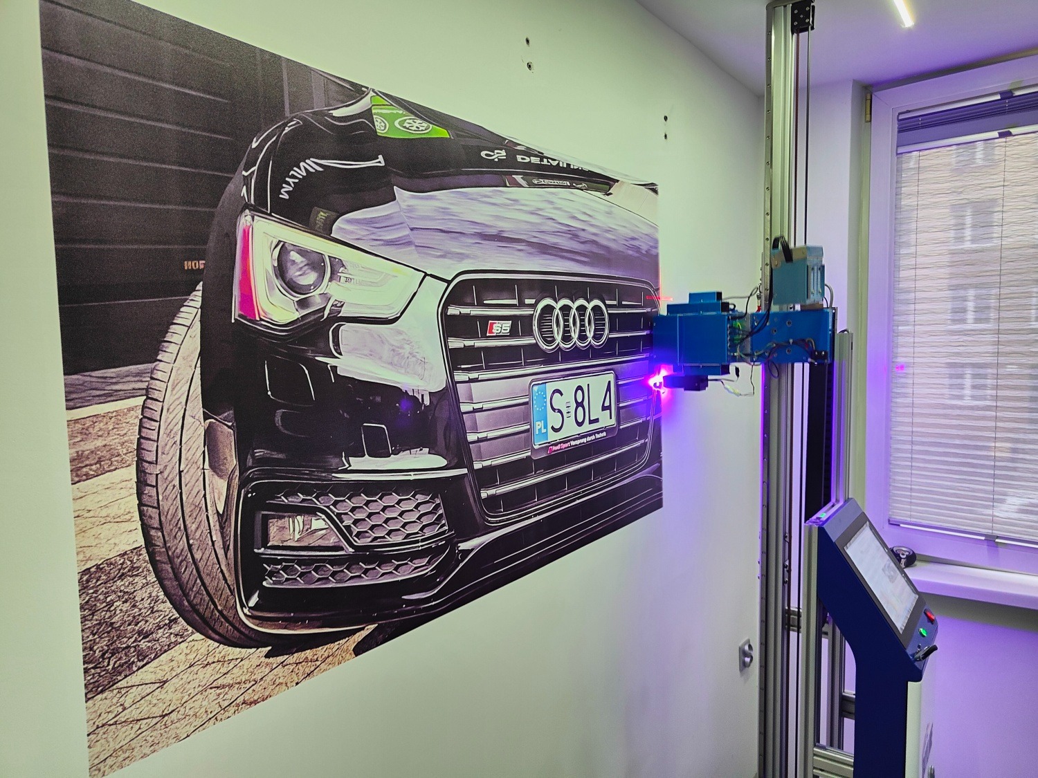 Drukarka ścienna w trakcie nanoszenia grafiki samochodu Audi S5 na ścianę. Widoczny laser i fragment okna w tle. Nowoczesna technologia druku.
