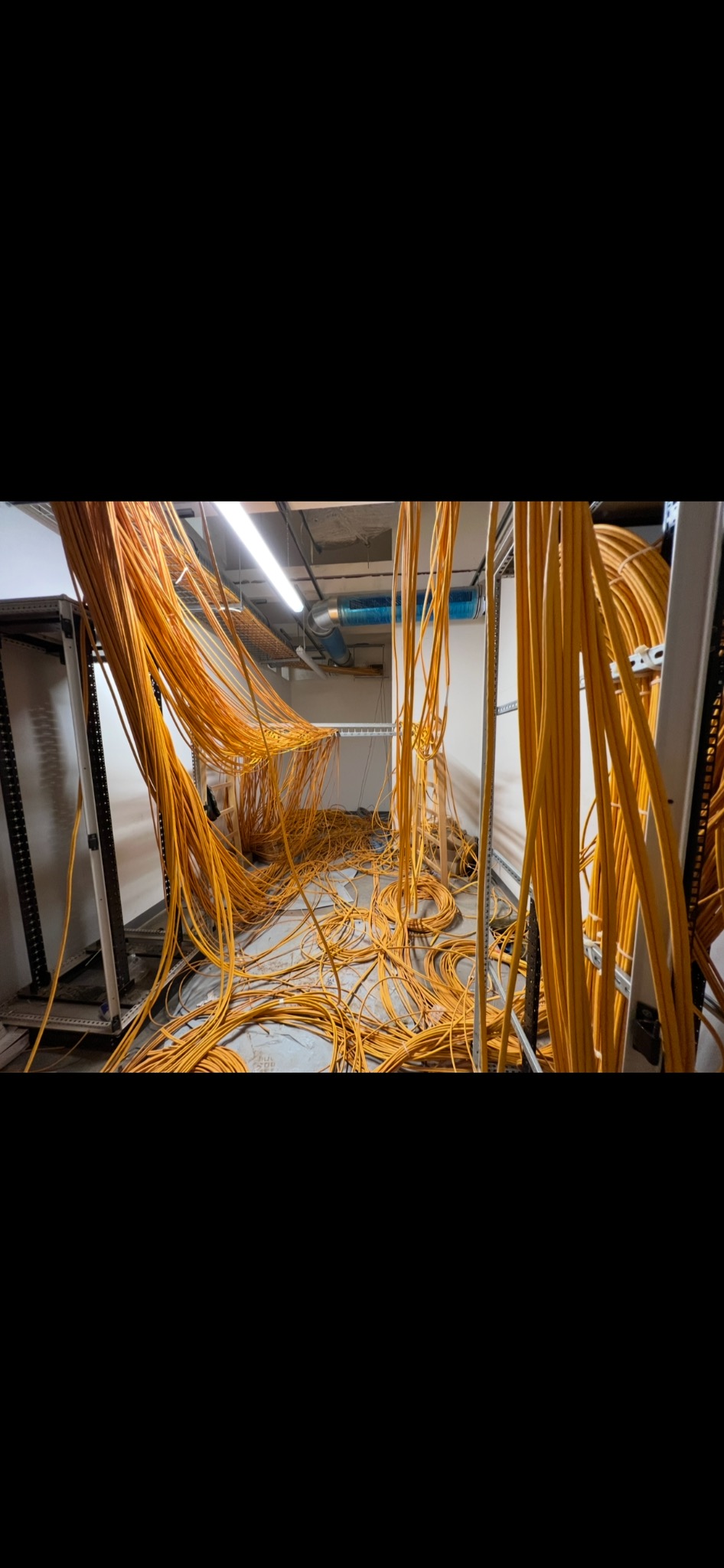 Rozciągnięte żółte kable w serwerowni w Zubrzycy Dolnej. Widok na metalowe stelaże i podwieszony system wentylacyjny. Etap prac instalacyjnych.