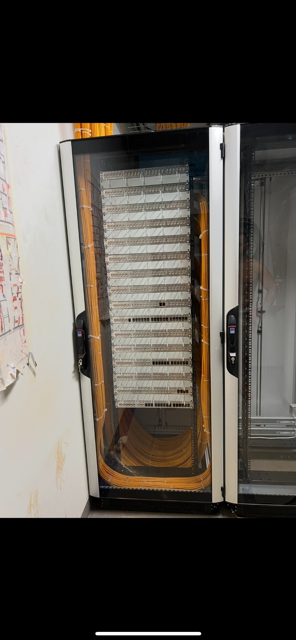 Otwarta szafa serwerowa z uporządkowanymi kablami światłowodowymi w kolorze pomarańczowym, widoczne panele krosownicze.