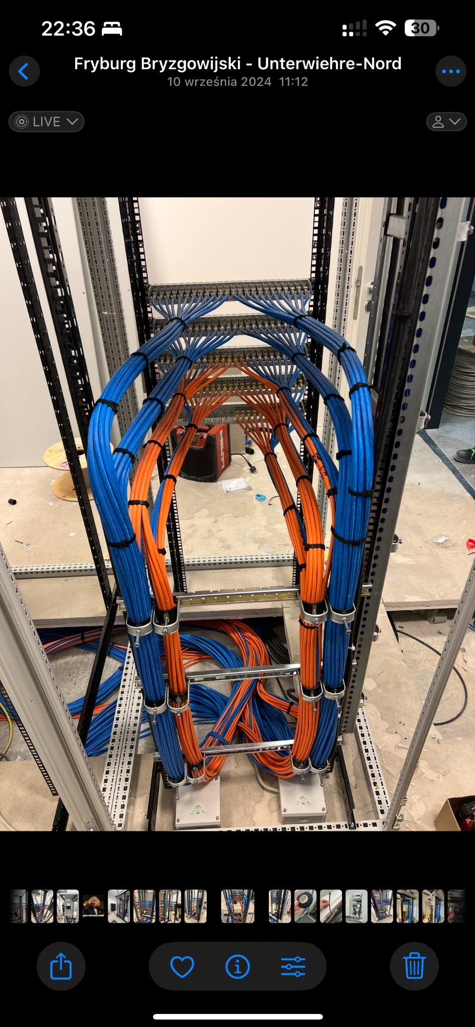 Profesjonalnie ułożone kable w szafie serwerowej, uporządkowane w wiązki niebieskie i pomarańczowe, zabezpieczone czarnymi opaskami zaciskowymi. Widoczne elementy konstrukcji szafy.