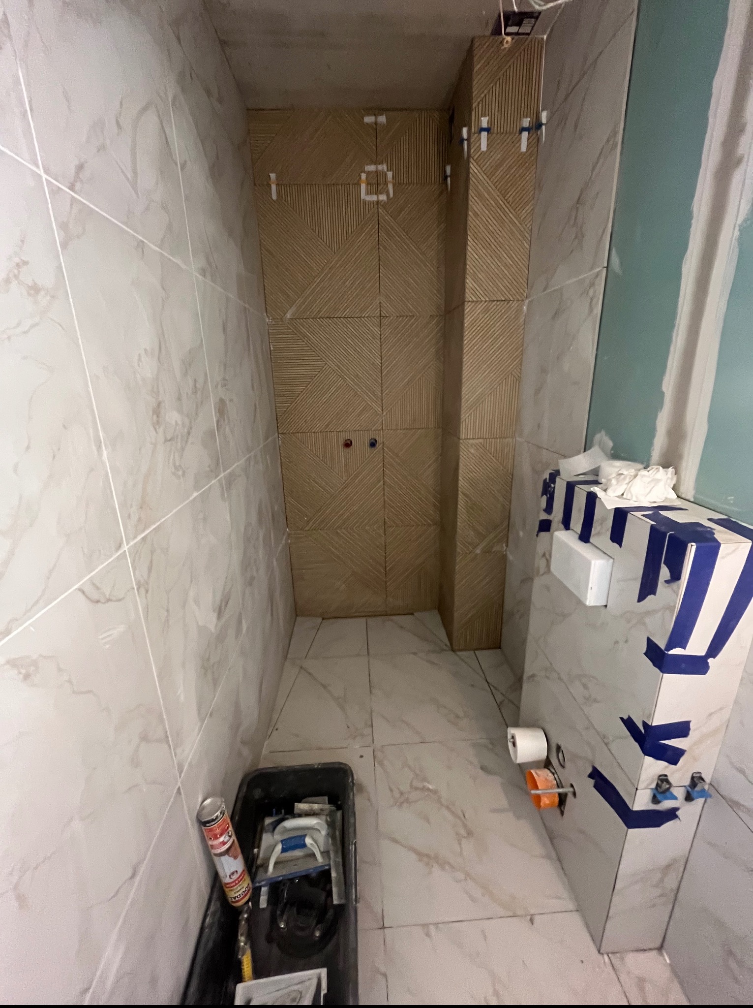 Wnętrze łazienki w trakcie wykańczania: marmurowe płytki na ścianach, dekoracyjne płytki na obudowie, narzędzia glazurnicze w kuwecie na podłodze.