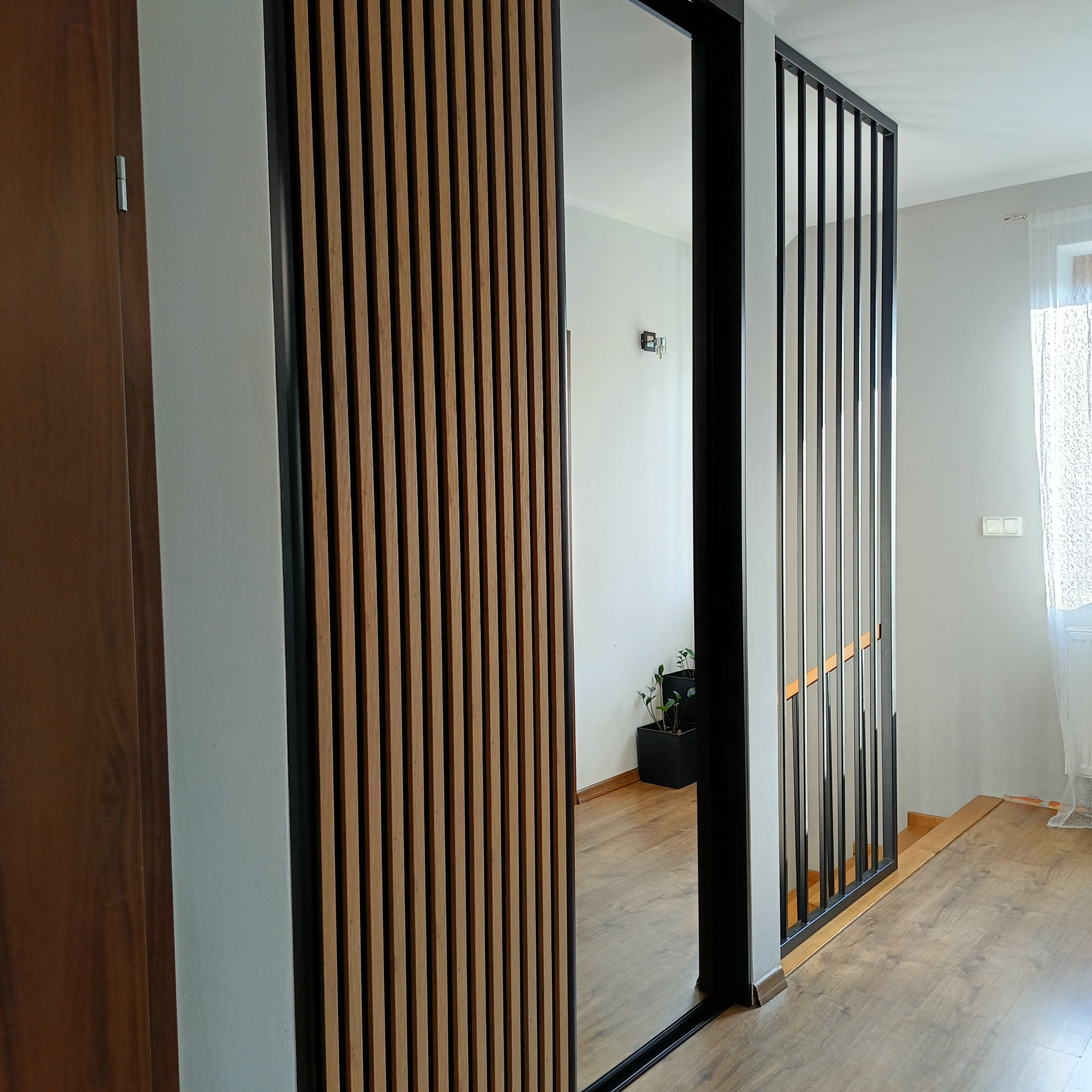 Nowoczesna zabudowa z drewnianych lameli i czarnych profili w Starym Mieście. Widoczne elementy drzwi i ażurowa ścianka działowa.