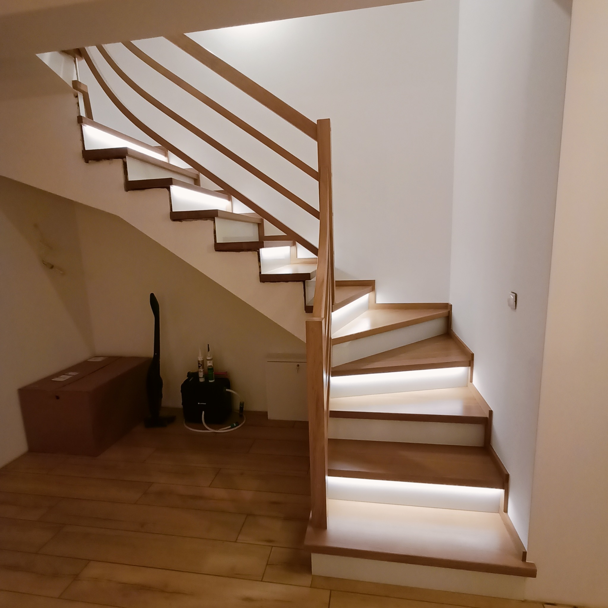 Drewniane schody z podświetleniem LED, widok z dołu. Jasne drewno i białe ściany tworzą nowoczesny design. Balustrada z prostych belek.